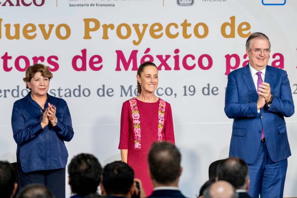 Tres personas en un evento relacionado con un nuevo proyecto de economía en México, con un fondo que muestra el logo del gobierno.
