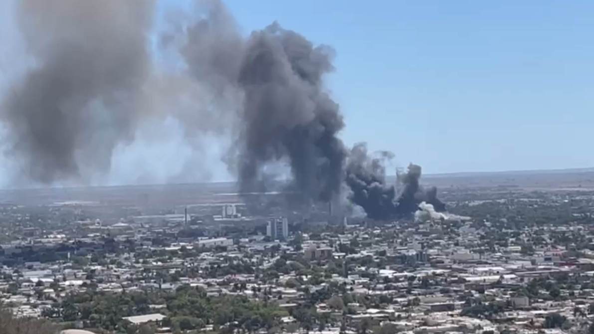 Vista panorámica de una ciudad con humo negro elevándose en el horizonte, indicando un posible incendio o explosión.