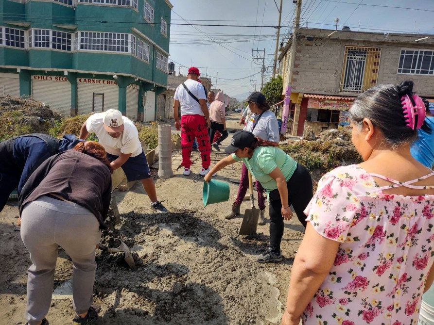 Grupo de personas trabajando en la calle, realizando labores de construcción. Algunos están cavando y otros vertiendo material en el suelo.