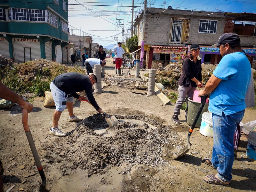 Grupo de personas trabajando en la construcción de una calle, con herramientas y materiales, en un entorno urbano.