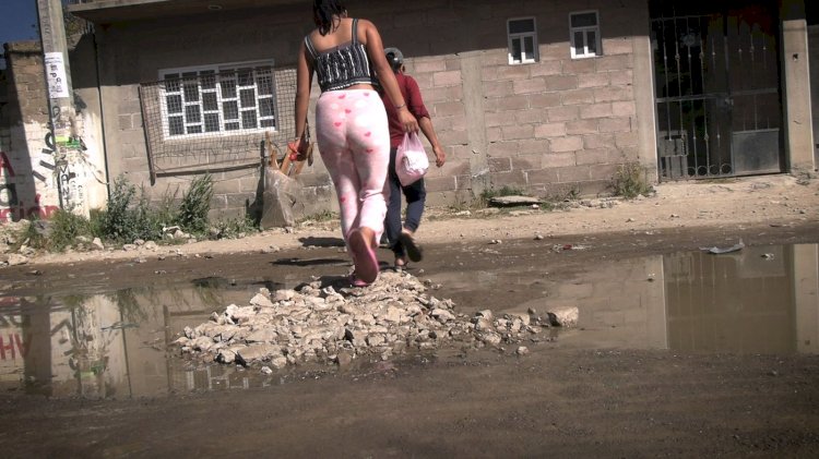 Una mujer camina sobre un montículo de escombros en una calle con agua estancada, mientras otra persona la sigue.