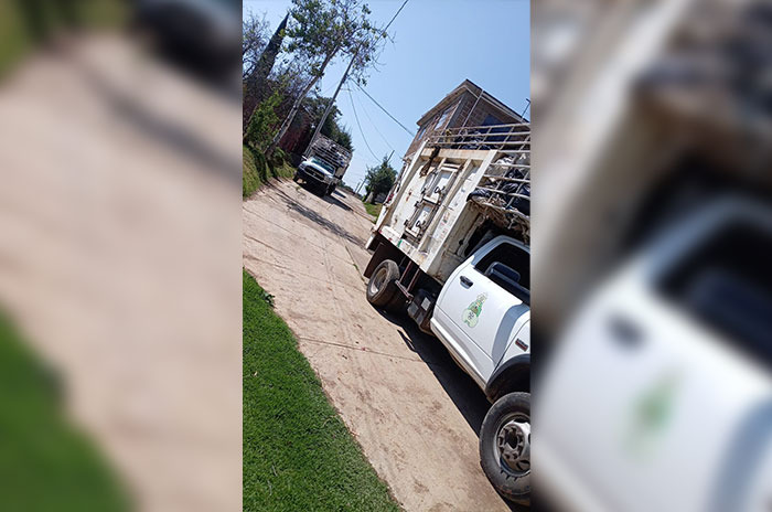 Camión de trabajo estacionado en una calle de tierra, con casas al fondo y vegetación a los lados.