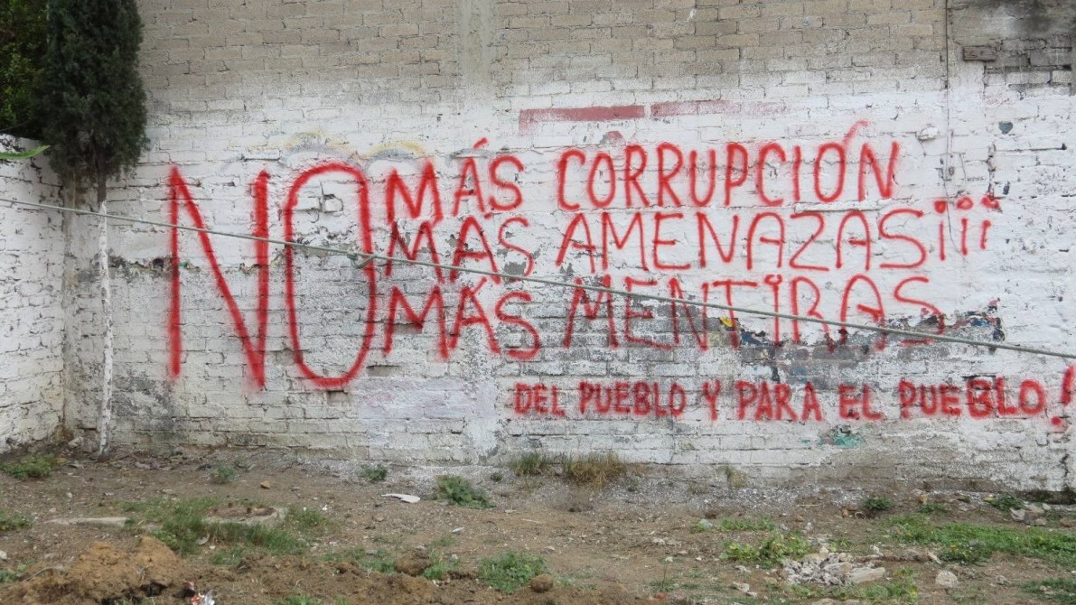 Graffiti on a wall reading 'NO más corrupción, más amenazas, más mentiras. Del pueblo y para el pueblo!' in red paint.