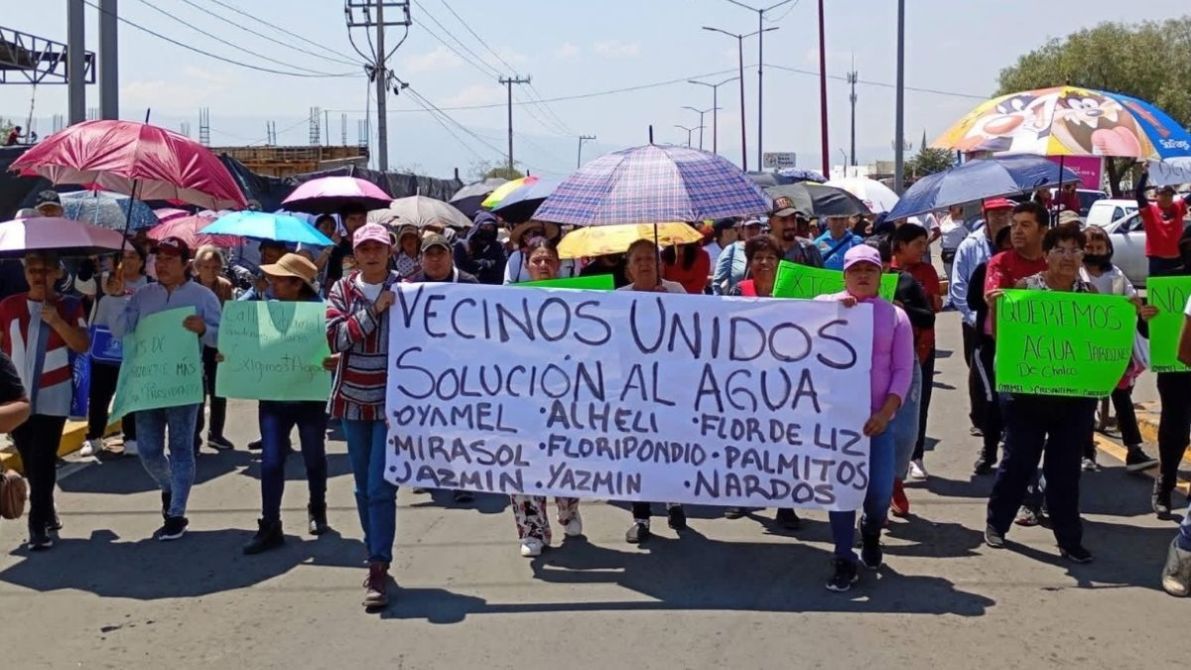 A crowd of people marching with umbrellas, holding banners and signs that demand solutions for water issues, with a focus on community unity.