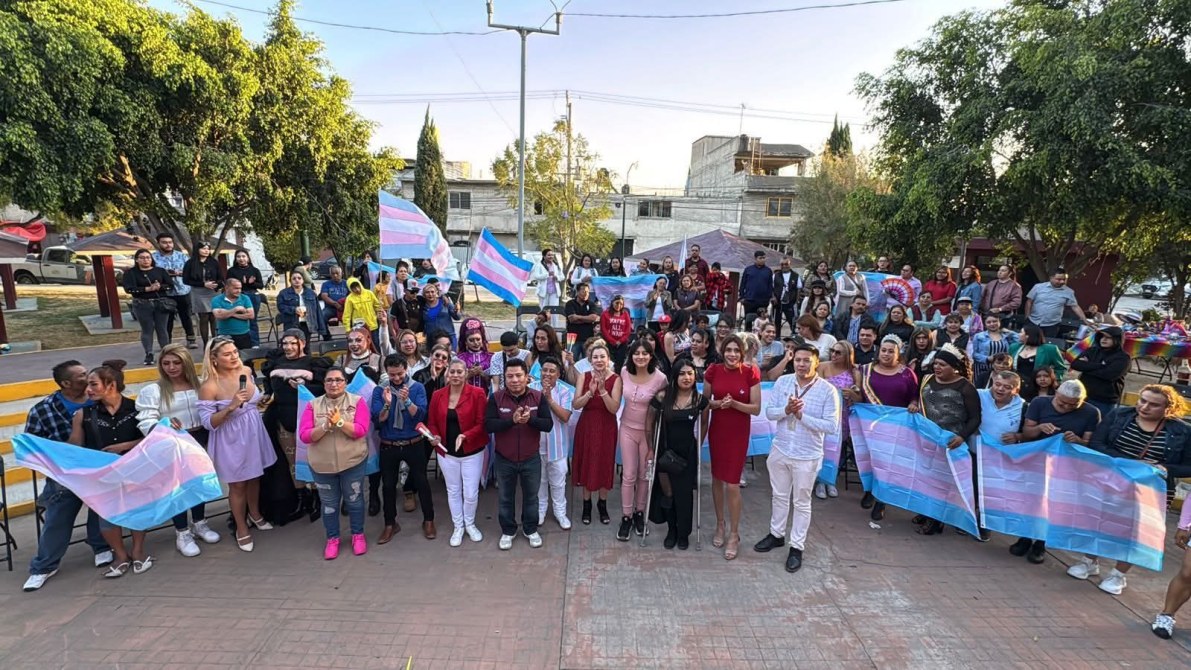 A large group of diverse individuals celebrating together outdoors, holding transgender pride flags, with a festive atmosphere and various colorful decorations.
