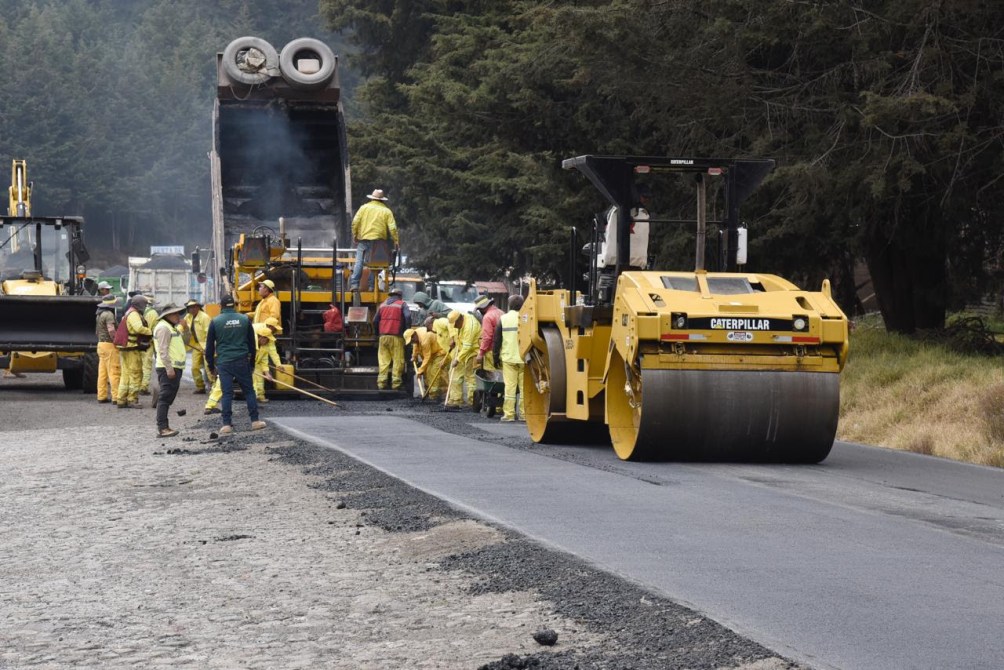 Obras de construcción de una carretera con un rodillo compactador y trabajadores en trajes de seguridad amarillos.