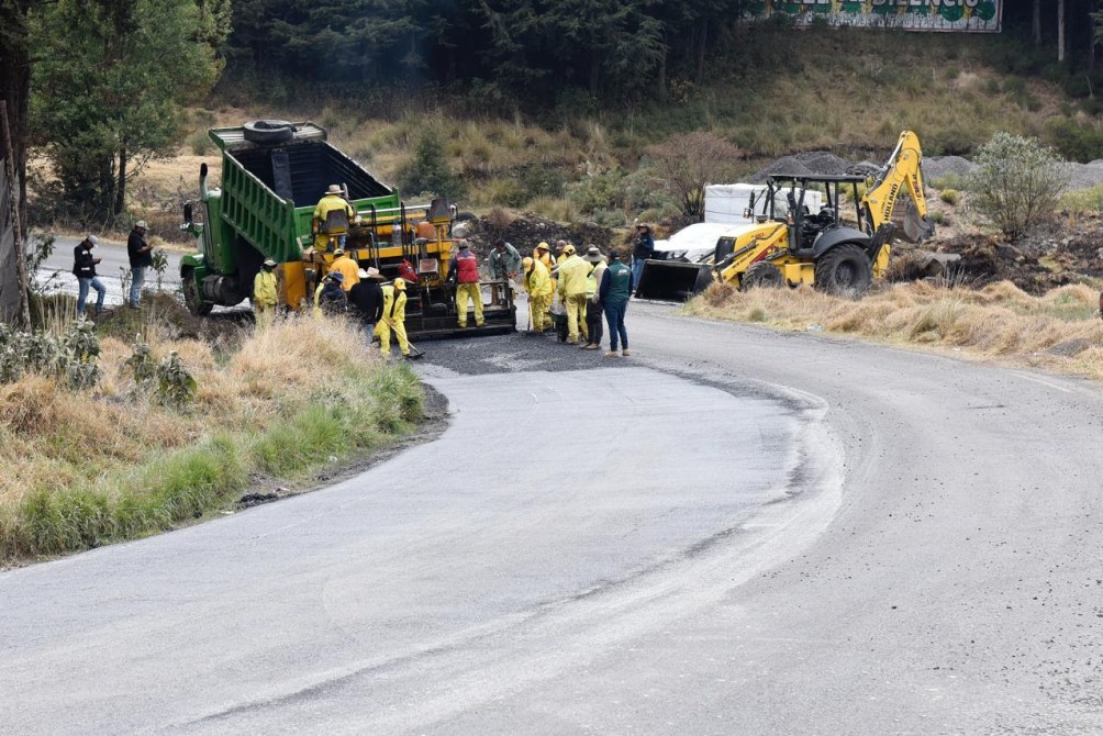 Trabajadores de la construcción realizando labores de pavimentación en una carretera, con maquinaria pesada en el sitio.