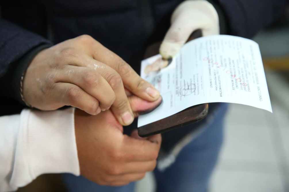 Una mano sosteniendo un documento mientras otra mano lo está firmando, con un fondo desenfocado.