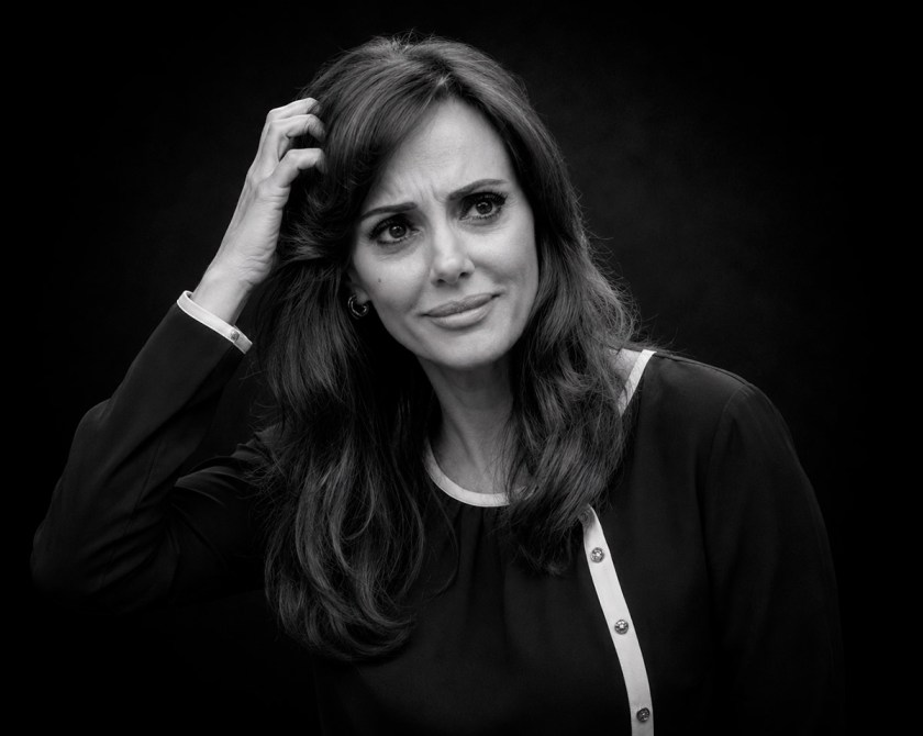Retrato en blanco y negro de una mujer con cabello largo y castaño, luciendo una expresión de confusión mientras se toca la cabeza.