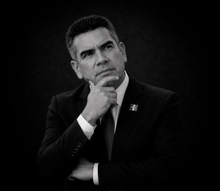 Retrato en blanco y negro de un hombre en traje, mirando hacia arriba con expresión pensativa y mano en la barbilla.