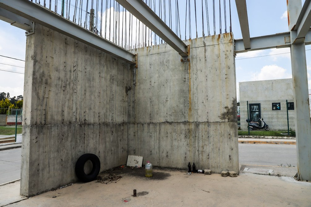 Interior de una estructura de concreto con paredes desnudas, un neumático en el suelo y algunos objetos desordenados. Se observa una motocicleta estacionada afuera.