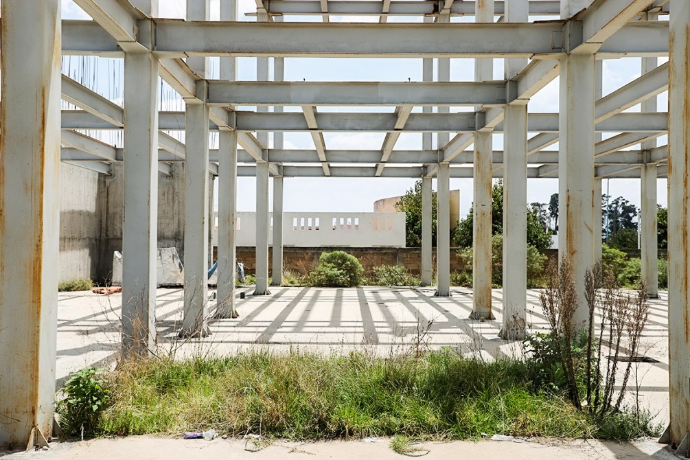 Estructura de construcción abandonada con columnas de acero y vegetación crecida en el suelo.