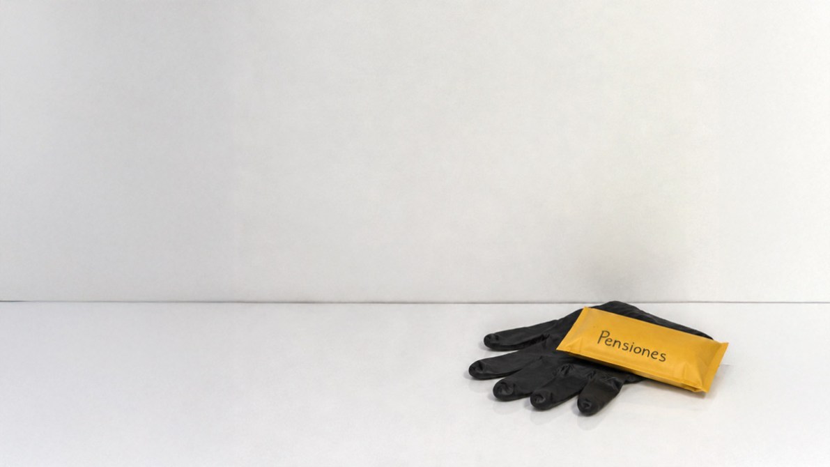 Un par de guantes negros sobre una superficie blanca, junto a un paquete amarillo con la palabra 'Pensiones'.