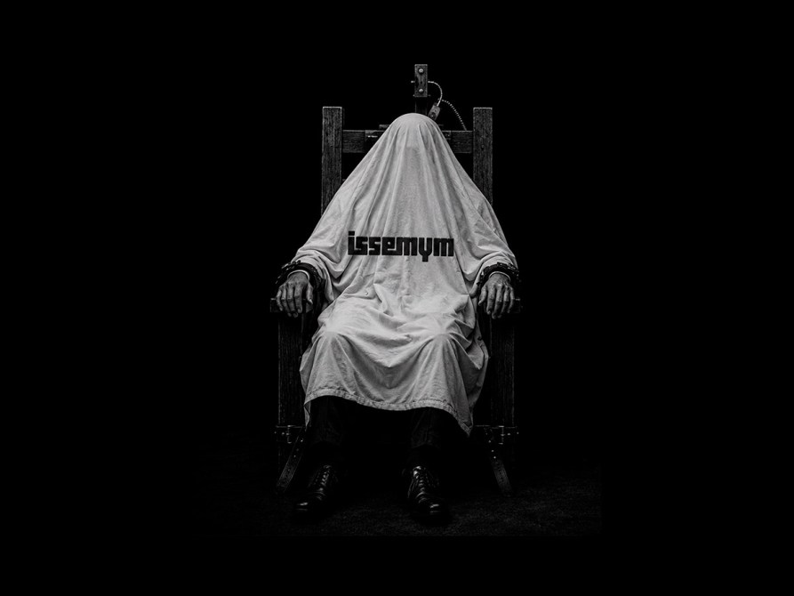 Persona con una sábana blanca sentada en una silla en un entorno oscuro, con texto 'issemy' sobre la sábana.