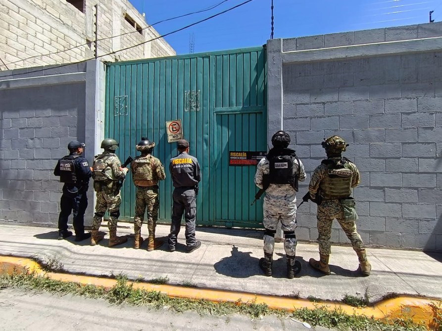 Grupo de policías y militares frente a una puerta verde con señales de advertencia.