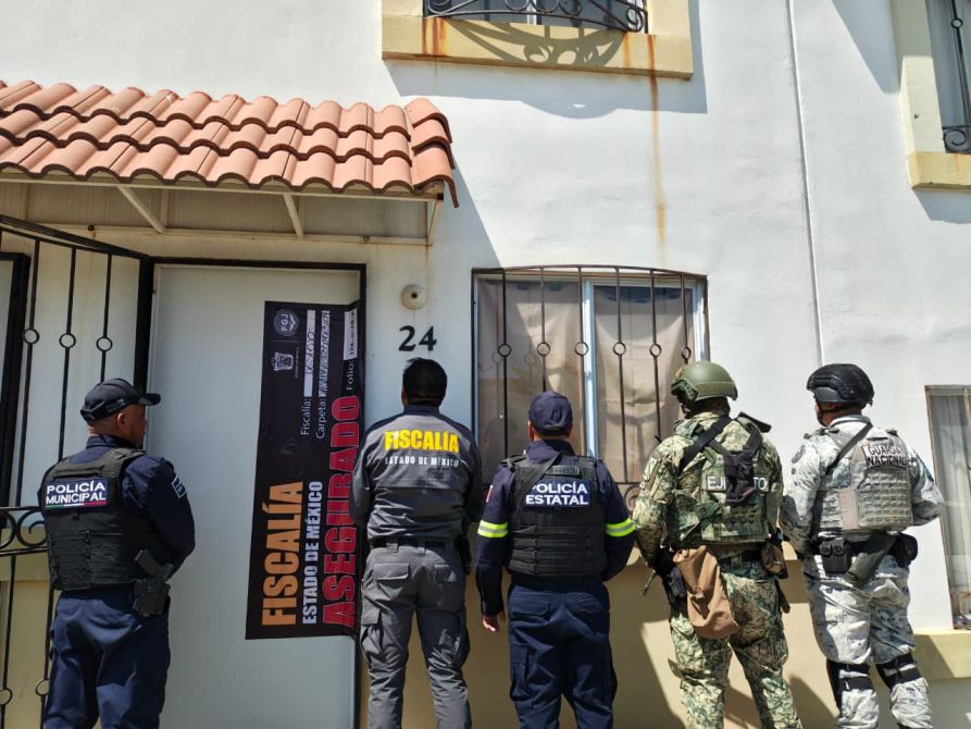 Grupo de policías y militares frente a una casa con un letrero de 'Fiscalía Estado de México Asegurado'.