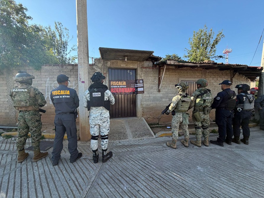 Un grupo de oficiales de seguridad, incluidos elementos de la Marina y la fiscalía, está parado frente a una puerta marcada con un cartel de 'Fiscalía' en un entorno urbano.