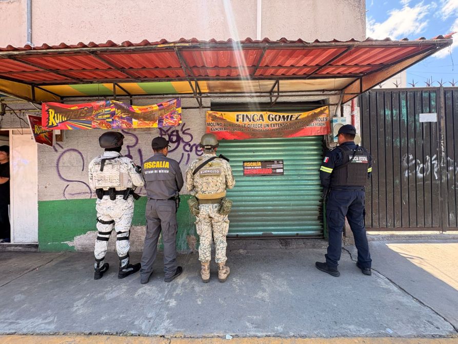 Cuatro agentes de la policía y el ejército frente a un negocio cerrado con una persiana verde, visible un letrero que dice 'FINCA GOMÉZ'.