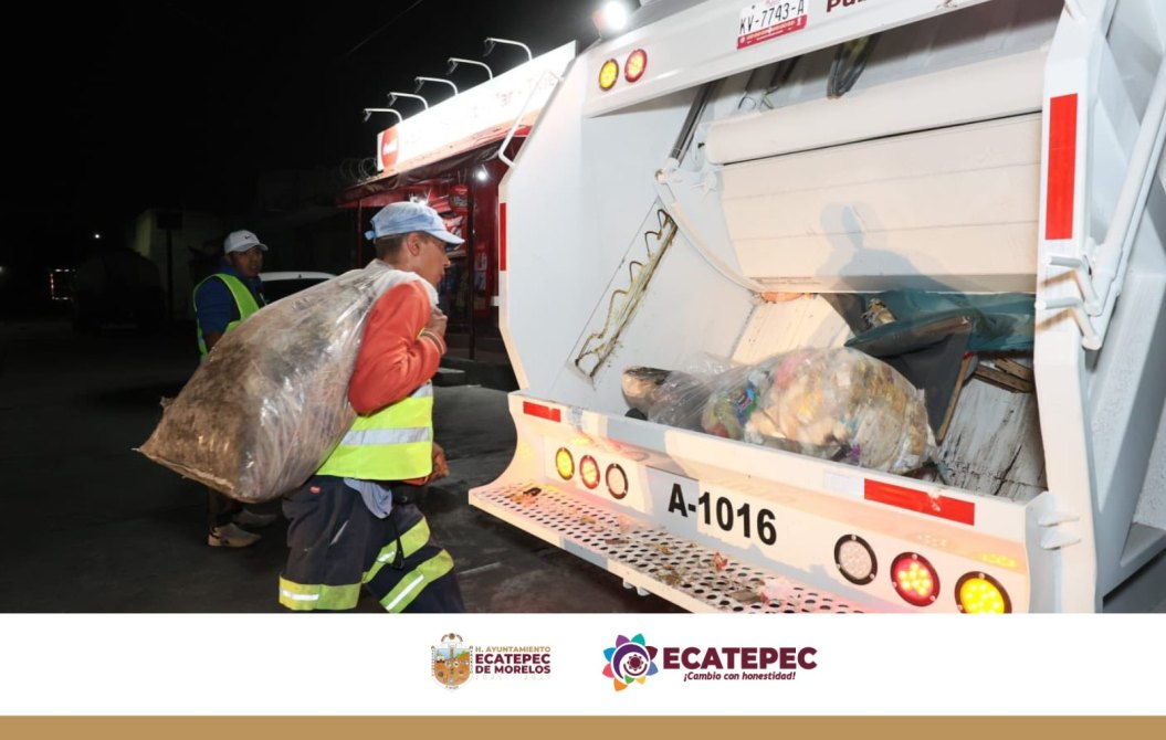 Dos trabajadores de recolección de basura cargando bolsas de desechos hacia un camión recolector en la noche.