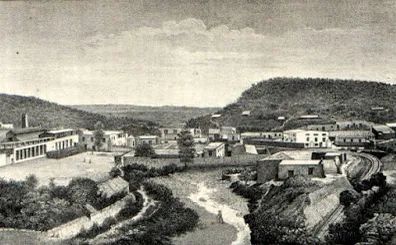 Vista panorámica de un pueblo con casas y montañas al fondo, rodeado de vegetación.