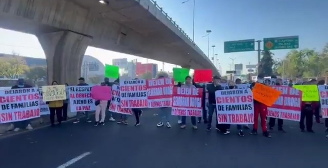 Protesta de personas sosteniendo carteles que exigen el respeto a los derechos laborales, bloqueando una carretera.