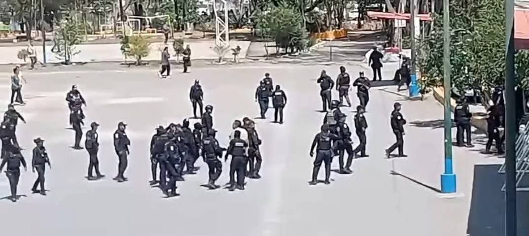 Grupo de policías en uniforme negro en un área abierta, algunos conversando y otros en movimiento.