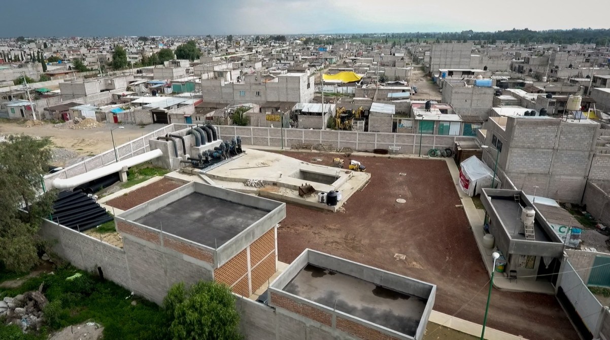Vista aérea de un área urbana con edificios de concreto, tuberías y un sistema de tratamiento de aguas residuales en primer plano.