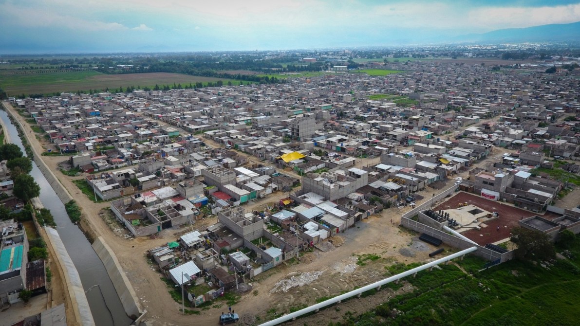 Vista aérea de un área urbana con viviendas de construcción simple y calles angostas, junto a un canal de agua.