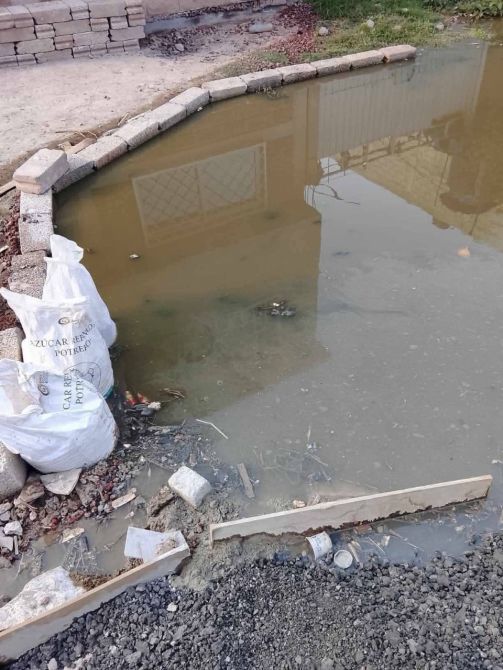 Charca de agua estancada con desechos y bolsas blancas en el borde, rodeada de bloques de piedra.