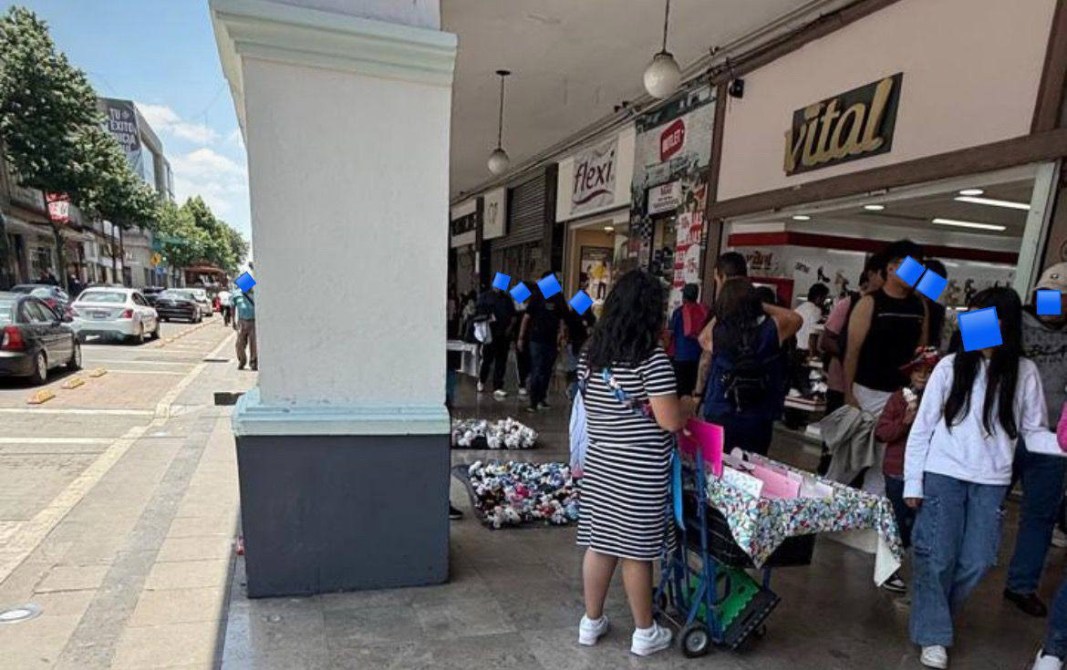 Vista de una calle con tiendas, personas caminando y un carrito con productos en primer plano.