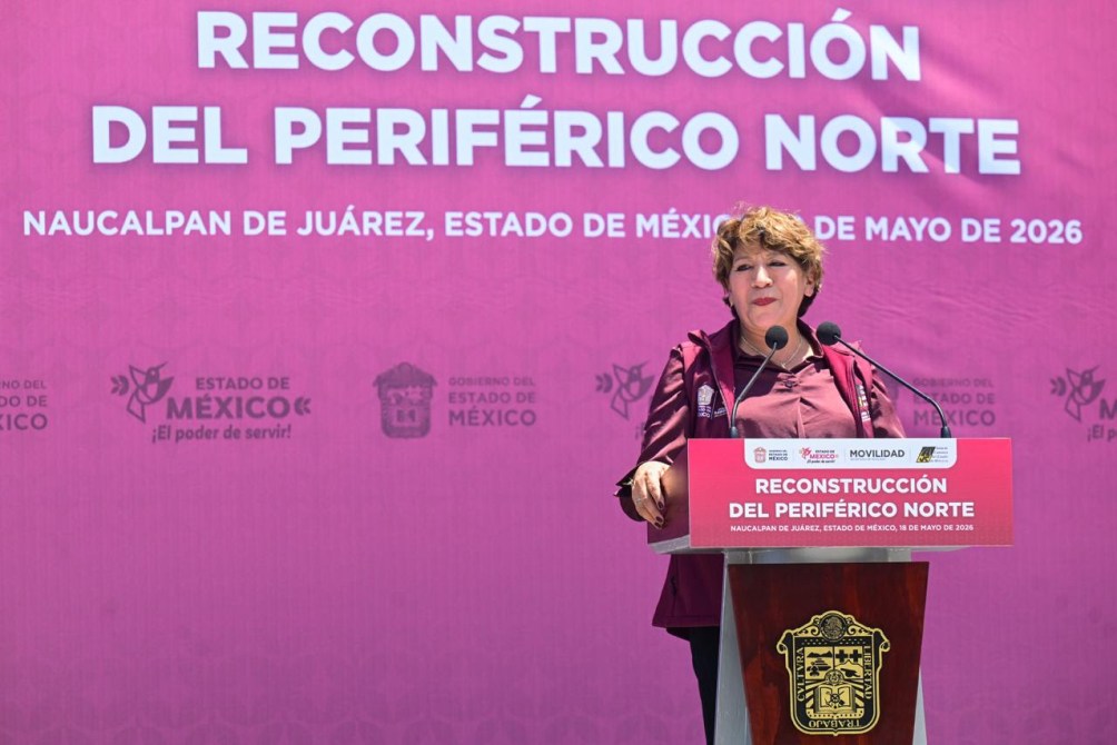 A woman speaking at a podium during a press conference about the Reconstruction of Periférico Norte in Naucalpan de Juárez, Mexico, on May 18, 2026. The backdrop features large text announcing the event and various logos.