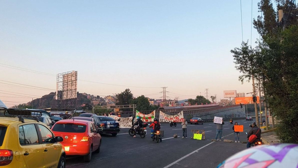 Protesta en una carretera con vehículos detenidos y pancartas visibles en el camino.