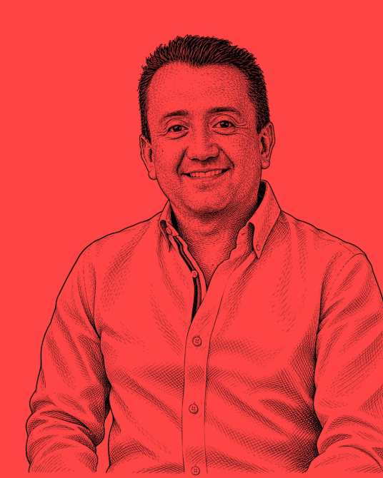 Retrato de un hombre sonriendo, vestido con una camisa clara, sobre un fondo rojo.
