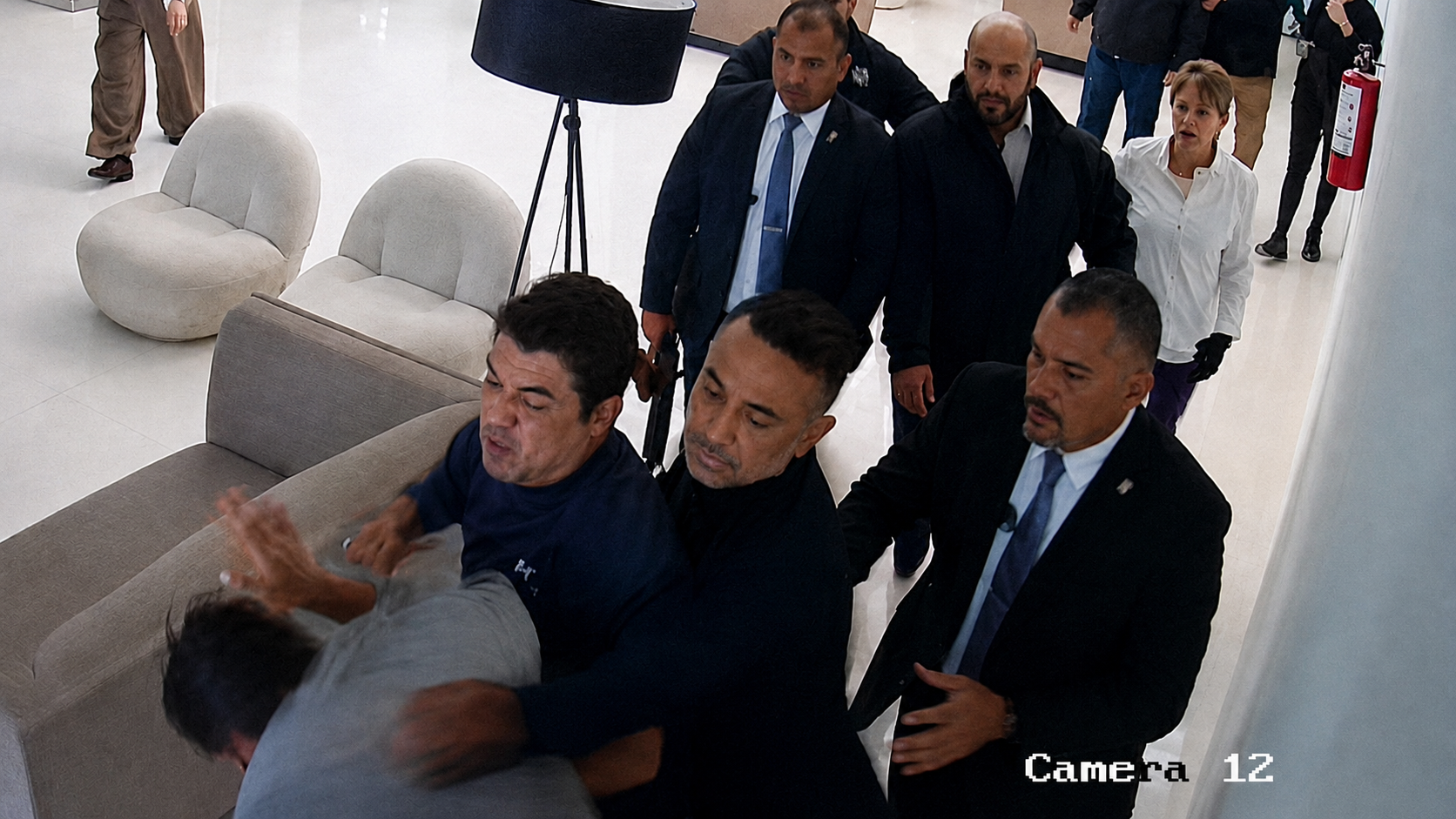 Imagen de videovigilancia que muestra a varias personas involucradas en una confrontación dentro de un inmueble. Se observa a un grupo de hombres sujetando a otra persona mientras varios individuos observan la escena en un pasillo interior.