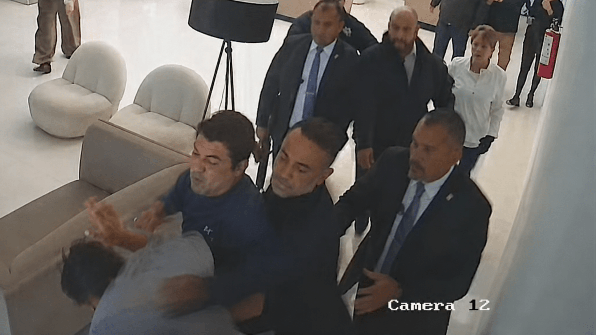 magen de videovigilancia que muestra a varias personas involucradas en una confrontación dentro de un inmueble. Se observa a un grupo de hombres sujetando a otra persona mientras varios individuos observan la escena en un pasillo interior.