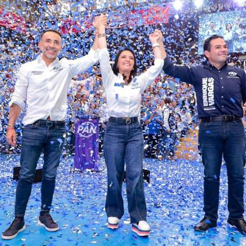 Fernando Flores, alcalde de Metepec, aparece junto a su esposa Iraí Albarrán y el senador Enrique Vargas durante un evento masivo del PAN. Los tres levantan las manos sobre un escenario mientras cae confeti azul y blanco frente a cientos de simpatizantes.