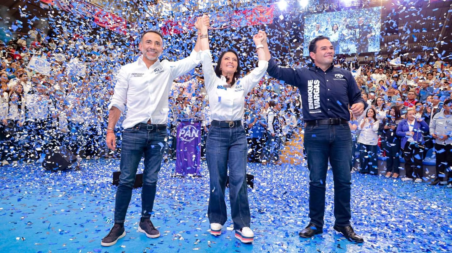 Fernando Flores, alcalde de Metepec, aparece junto a su esposa Iraí Albarrán y el senador Enrique Vargas durante un evento masivo del PAN. Los tres levantan las manos sobre un escenario mientras cae confeti azul y blanco frente a cientos de simpatizantes.