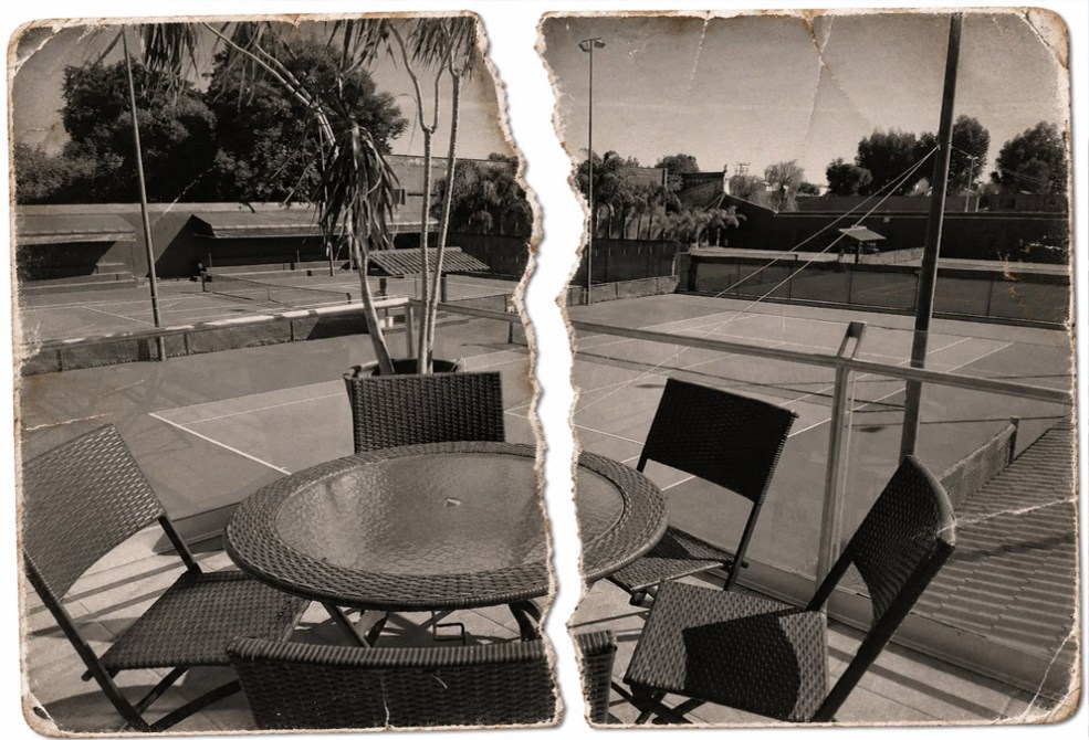 Vista de una terraza con mesas y sillas de mimbre, con canchas de tenis al fondo, en una imagen en blanco y negro.